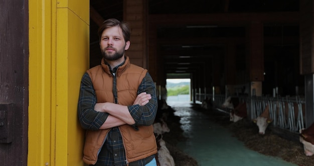 Porträt eines gutaussehenden jungen Landwirts in Hemd und orangefarbener Weste, der im Hintergrund der Milchfarm in die Kamera blickt Landwirtschaftskonzept für die Landwirtschaft