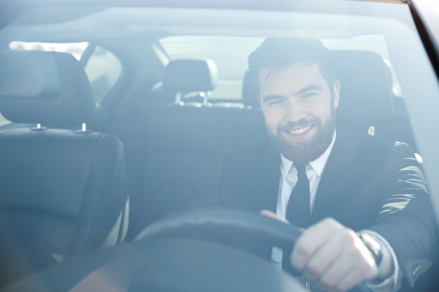 Porträt eines gutaussehenden lächelnden Geschäftsmannes, der sein Auto fährt