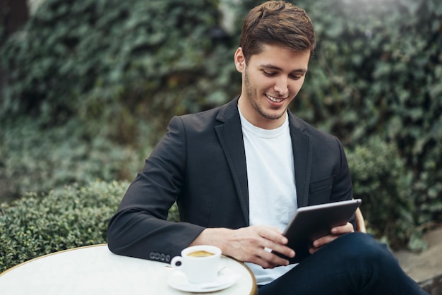 Porträt eines gutaussehenden, lächelnden kaukasischen Geschäftsmannes, der während der Kaffeepause im modernen Café in der Stadt ein Tablet-Gerät hält, das im Internet surft und gute Nachrichten in E-Mails liest Technologie-Geschäftskonzept