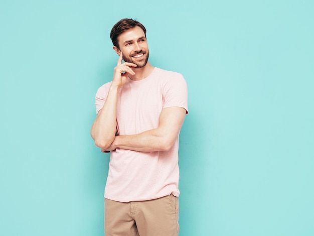 Porträt eines gutaussehenden, lächelnden, stilvollen Hipster-Lambersexual-Modells Sexy Mann in rosafarbenem T-Shirt und Hose Mode männlich isoliert auf blauer Wand im Studio