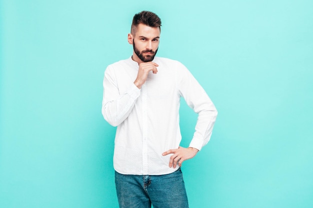 Porträt eines gutaussehenden, lächelnden, stilvollen Hipster-Lambersexual-ModelsMann in weißem Pullover und Jeans Modemann isoliert auf blauer Wand im Studio