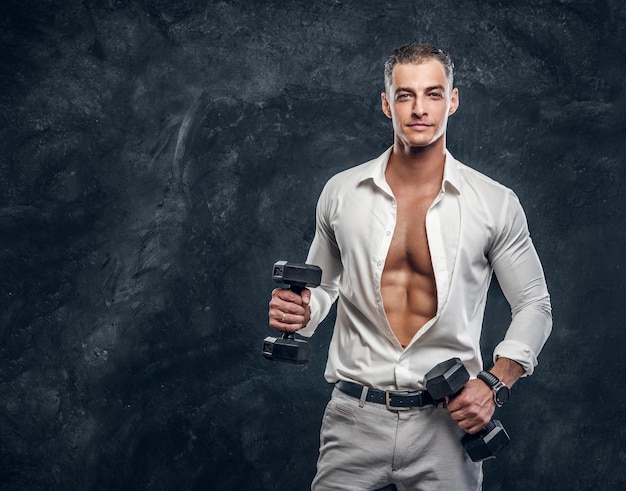 Porträt eines gutaussehenden muskulösen Mannes mit Hanteln im weißen Hemd im dunklen Fotostudio.