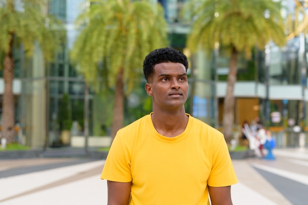 Porträt eines gutaussehenden schwarzen afrikanischen Mannes, der im Sommer ein gelbes T-Shirt im Freien in der Stadt trägt, während er nachdenkt