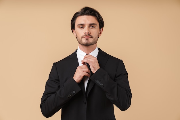 Porträt eines gutaussehenden, selbstbewussten jungen Geschäftsmannes im Anzug, der isoliert über beige Wand steht und posiert