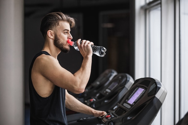 Porträt eines gutaussehenden Sportlers, der Cardio-Training macht und Wasser im Fitnessstudio trinkt