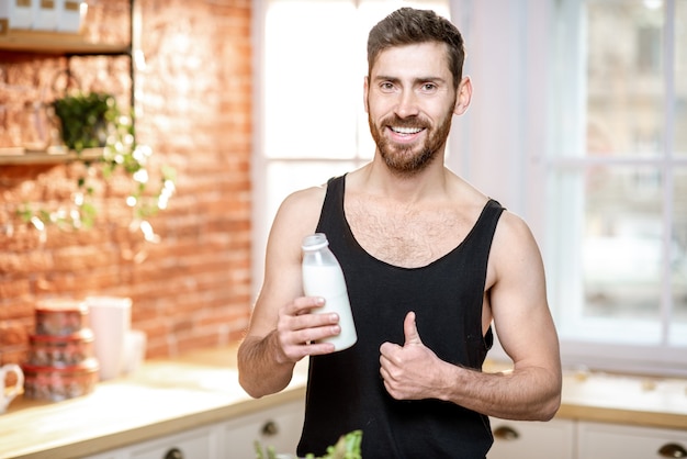 Porträt eines gutaussehenden Sportlers im schwarzen T-Shirt, der Milchshake in der Küche zu Hause trinkt