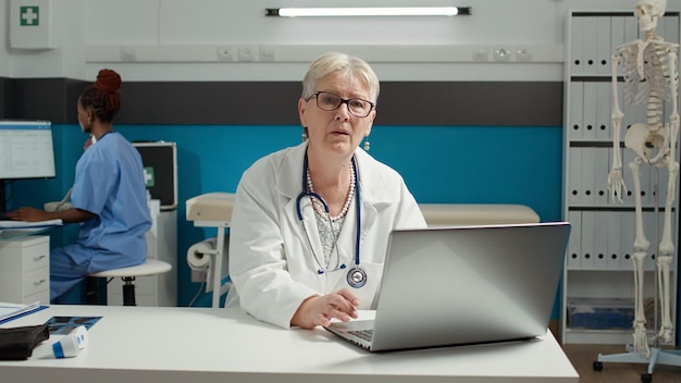 Porträt eines Hausarztes, der einen Laptop bei der Gesundheitsuntersuchung verwendet und an Terminunterlagen arbeitet. Ärztin, die Diagnoseergebnisse im medizinischen System online betrachtet.
