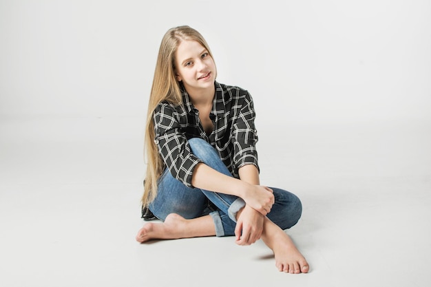 Porträt eines hellhäutigen Mädchens mit langen blonden Haaren in Hemd und Jeans auf weißem Hintergrund