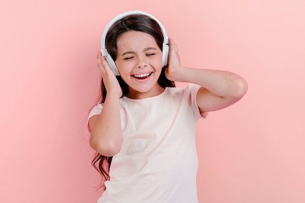 Porträt eines herrlichen kleinen Mädchens mit geschlossenen Augen in den Kopfhörern hörend Musik und singen berührt ihren Kopf