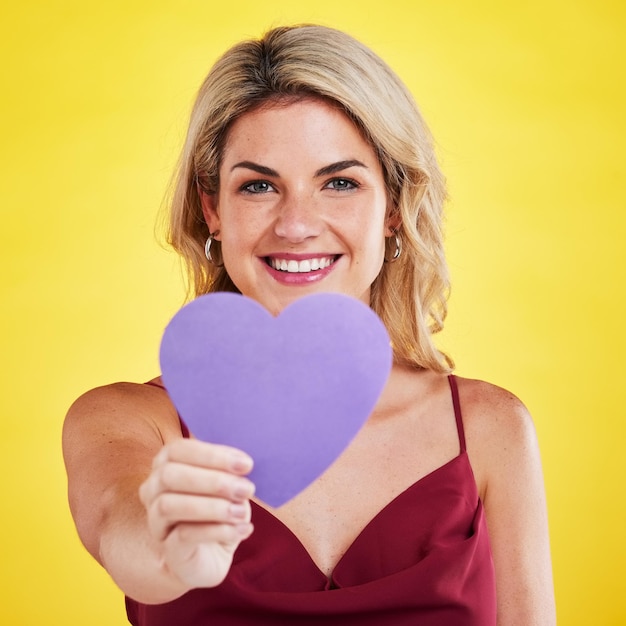 Porträt eines Herzens und einer Frau mit Wellness-Emoji und Glück vor einem Studiohintergrund. Gesicht eines weiblichen Models und einer glücklichen Dame mit einem Symbol für Liebeszeichen und Unterstützung mit einem romantischen und fürsorglichen Lächeln