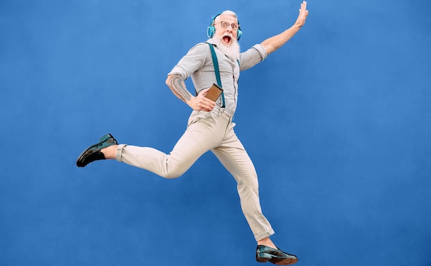 Porträt eines hipster älteren Mannes, der gegen blauen Hintergrund springt