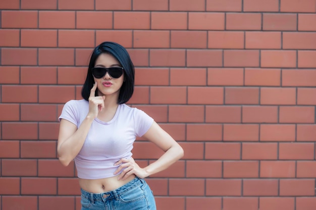 Porträt eines Hipster-Mädchens auf Backsteinmauerhintergrund Schöne asiatische Frau posiert für ein Foto