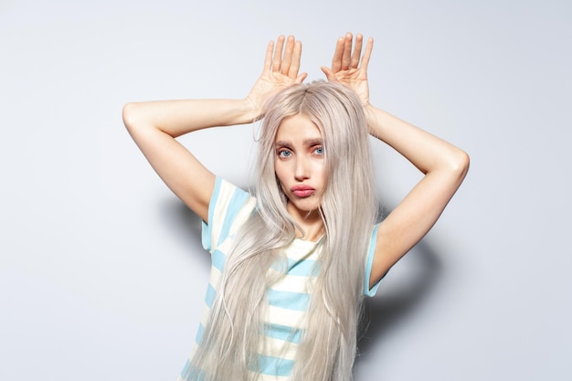 Porträt eines hübschen blonden Mädchens, das Hasenohren mit den Händen auf weißem Hintergrund zeigt