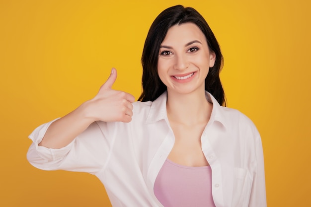 Porträt eines hübschen entzückenden positiven Mädchens, das Daumen auf gelbem Hintergrund hochhebt