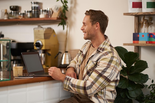 Porträt eines hübschen Geschäftsmanns, eines jungen digitalen Nomaden, der in einem Café sitzt und auf seinen Laptop schaut