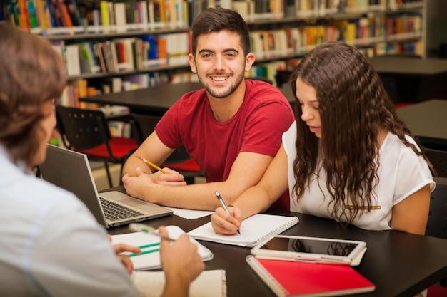 Foto porträt eines hübschen hispanischen jungen mannes, der mit einigen seiner freunde in der bibliothek studiert