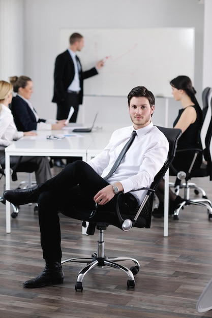 Porträt eines hübschen jungen Geschäftsmannes mit Leuten im Hintergrund bei der Bürositzung
