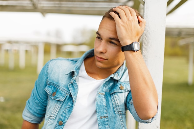 Porträt eines hübschen jungen Mannes in Jeanskleidung mit einer schwarzen Uhr auf Natur