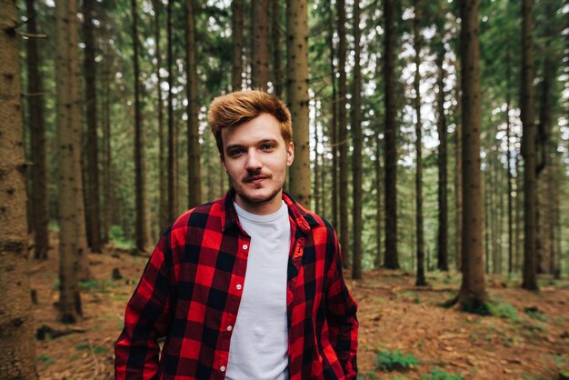 Porträt eines hübschen jungen Mannes in Rot, der in einem Nadelwald steht und für die Kamera posiert