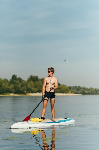 Porträt eines hübschen jungen Mannes mit sportlichem Oberkörper, der an einem sonnigen Tag auf dem Fluss steht