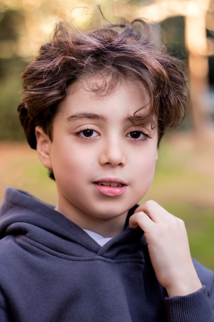 Porträt eines hübschen Jungen mit langen blonden Haaren im Garten, der lächelnd in die Kamera blickt