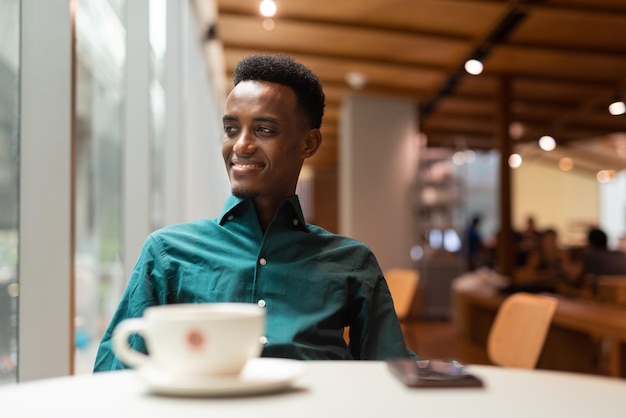 Porträt eines hübschen jungen schwarzen Mannes im Café, der durch das Fenster schaut