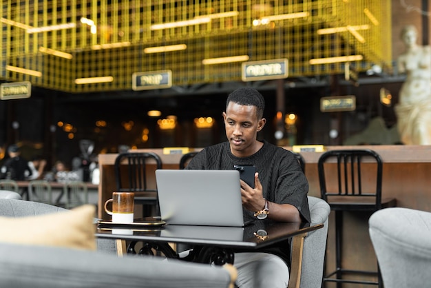 Porträt eines hübschen jungen schwarzen Mannes mit Laptop-Computer im Café