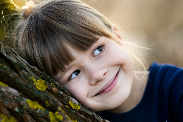 Porträt eines hübschen Kindermädchens, das an einem Baumstamm im Herbst draußen lehnt.