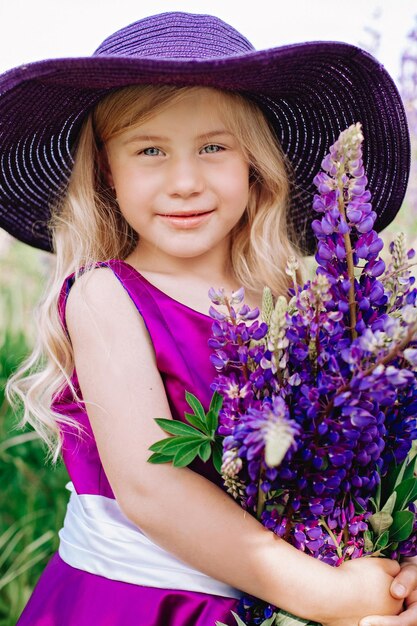 Porträt eines hübschen Mädchens mit violettem Hut mit Lupinensträußen im Gesicht