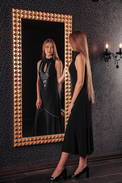 Porträt eines hübschen, süßen Teenager-Mädchens in einem eleganten Kleid am Spiegel