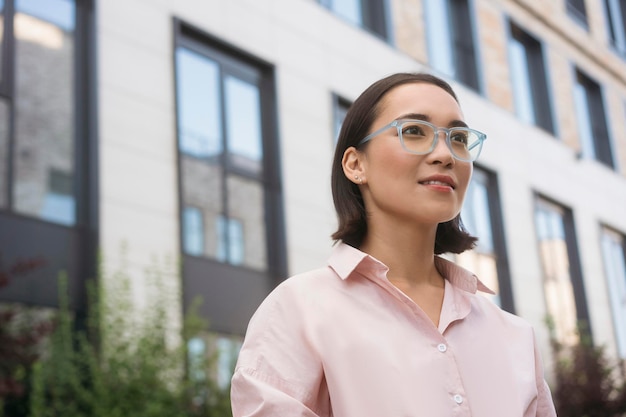 Porträt eines intelligent lächelnden asiatischen Studenten mit stilvoller Brille, der auf dem Universitätscampus steht