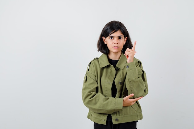 Porträt eines jugendlichen Mädchens, das in einer grünen Armeejacke nach oben zeigt und eine intelligente Vorderansicht sieht