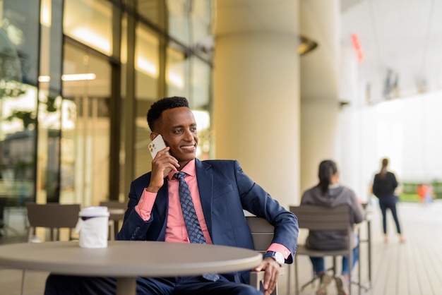 Porträt eines jungen afrikanischen Geschäftsmannes mit Anzug und Krawatte im Freien im Café
