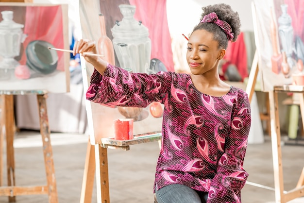 Porträt eines jungen afrikanischen Studenten, der im Atelier zum Malen sitzt