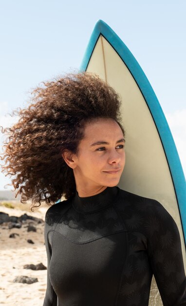 Porträt eines jungen Afro-Surfermädchens mit Surfbrett am Strand mit Neoprenanzug