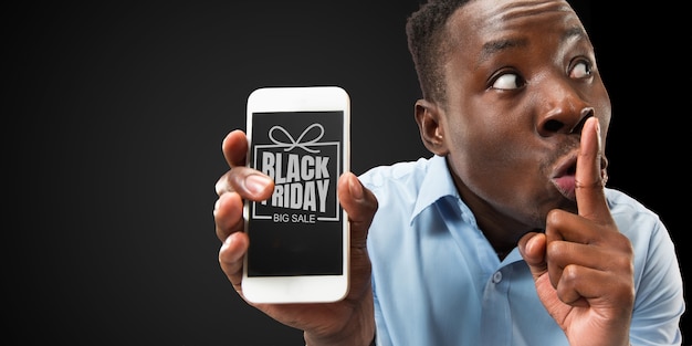 Porträt eines jungen Afroamerikaners, der Smartphone-Bildschirm auf schwarzem Hintergrund zeigt