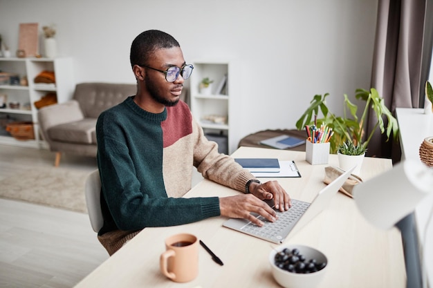 Porträt eines jungen afroamerikanischen Mannes, der eine Brille trägt, während er von zu Hause aus arbeitet und Laptop-Kopie verwendet ...