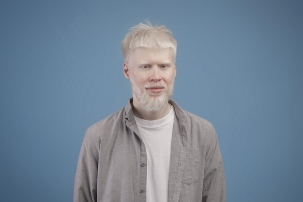 Porträt eines jungen Albino-Mannes mit weißem Haar, blasser Haut und blauen Augen, der in die Kamera gegen Blau blickt