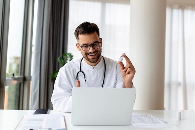 Porträt eines jungen Arztes, der mit einem Online-Patienten auf einem Laptop-Bildschirm spricht, der am Schreibtisch der Klinik sitzt und eine Online-Konsultation für eine häusliche Gesundheitsbehandlung anbietet Telemedizin Fernmedizin