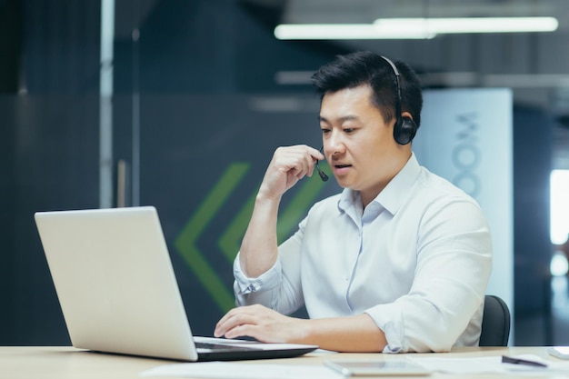 Porträt eines jungen asiatischen männlichen Beraters im Support-Service, der im Büro am Tisch sitzt