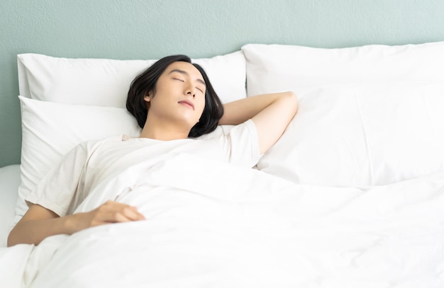 Porträt eines jungen asiatischen Mannes, der entspannt in einem gemütlichen weißen Bett schläft und die Augen geschlossen hält, während er morgens mit einer Decke bedeckt ist Guy genießt süße Träume, friedliche Zeit und Energiekraftwiederherstellung