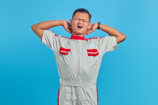 Porträt eines jungen asiatischen Mechanikers, der sich mit offenem Mund über blauem Hintergrund schläfrig fühlt