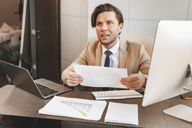 Porträt eines jungen attraktiven Geschäftsmannes, der seinen Krawattenständer in seinem Büro anpasst, nachdem er online war