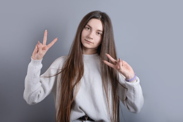 Porträt eines jungen attraktiven Mädchens mit dunklem langem Haar, das V Zeichen für Sieg oder Friedenszeichen sgesture