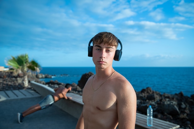 Porträt eines jungen attraktiven männlichen Sportlers ohne Hemd in einem Park mit Kopfhörern im Freien