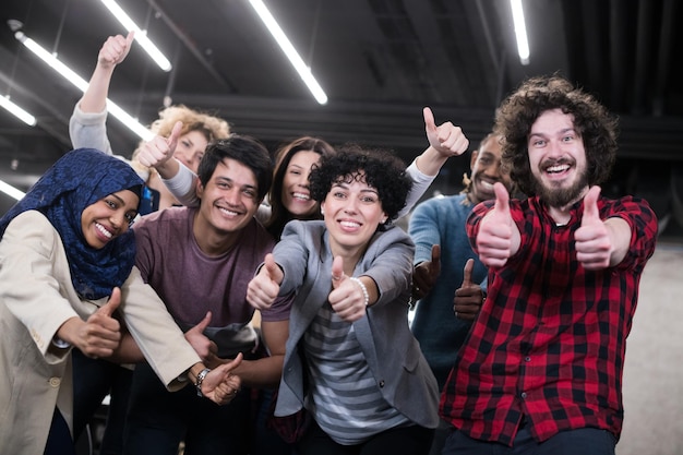 Porträt eines jungen aufgeregten multiethnischen Geschäftsteams von Softwareentwicklern, die stehen und in die Kamera schauen, während sie den Erfolg im modernen Startup-Büro feiern