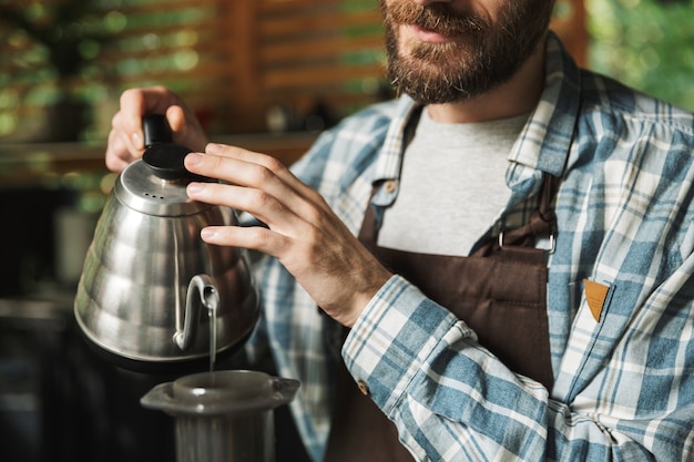 Porträt eines jungen Barista-Mannes mit Schürze, der Kaffee macht, während er im Straßencafé oder Kaffeehaus im Freien arbeitet?