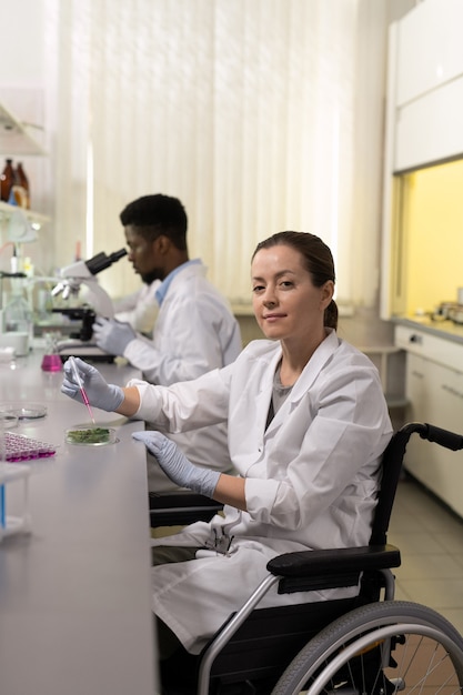 Porträt eines jungen behinderten Chemikers, der bei der Arbeit am Tisch im Labor in die Kamera schaut