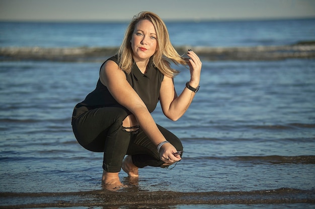 Porträt eines jungen blonden Mädchens, das am Meer mit abgenutzten Modeaccessoires posiert