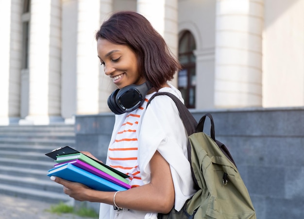 Porträt eines jungen College-Mädchens, das Ordner und Notizbücher hält und die Straße hinuntergeht, um zur Schule oder zum College zu gehen Studentin lächelnd und glücklich